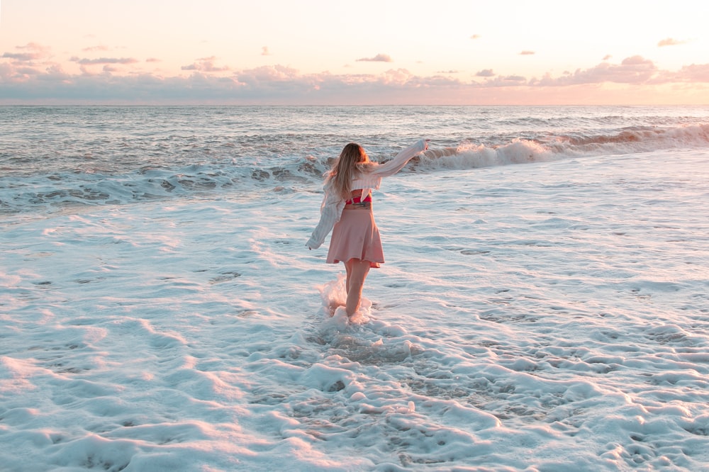 a woman in a pink dress standing in the surf