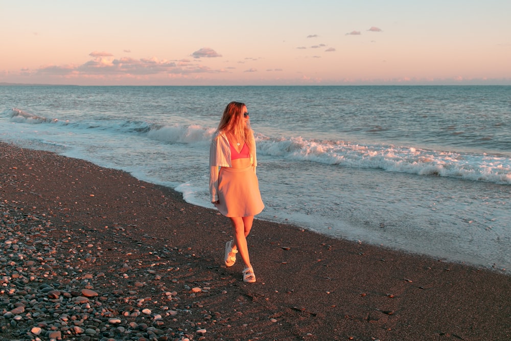 a woman walking along a beach next to the ocean