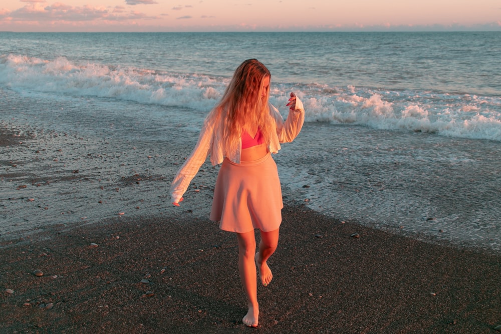 a woman in a pink dress is walking on the beach