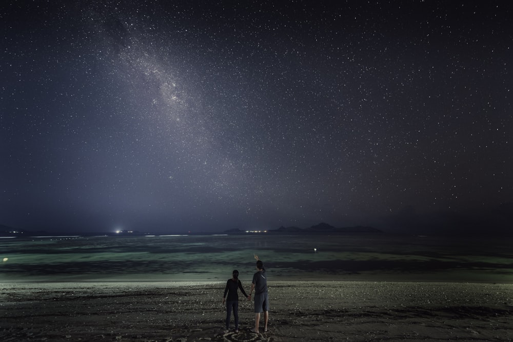 two people standing on a beach under a night sky
