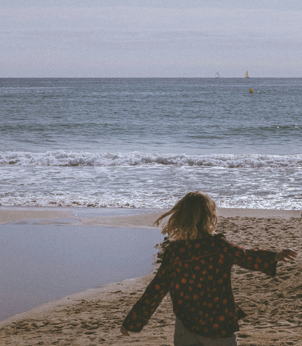 a woman standing on top of a sandy beach next to the ocean