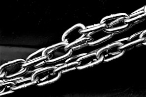 Metal chains with interconnected links are captured in a close-up perspective, highlighting their shine and texture against a dark background.