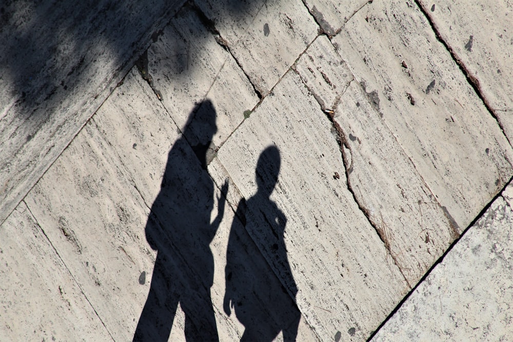 a shadow of two people walking down a sidewalk