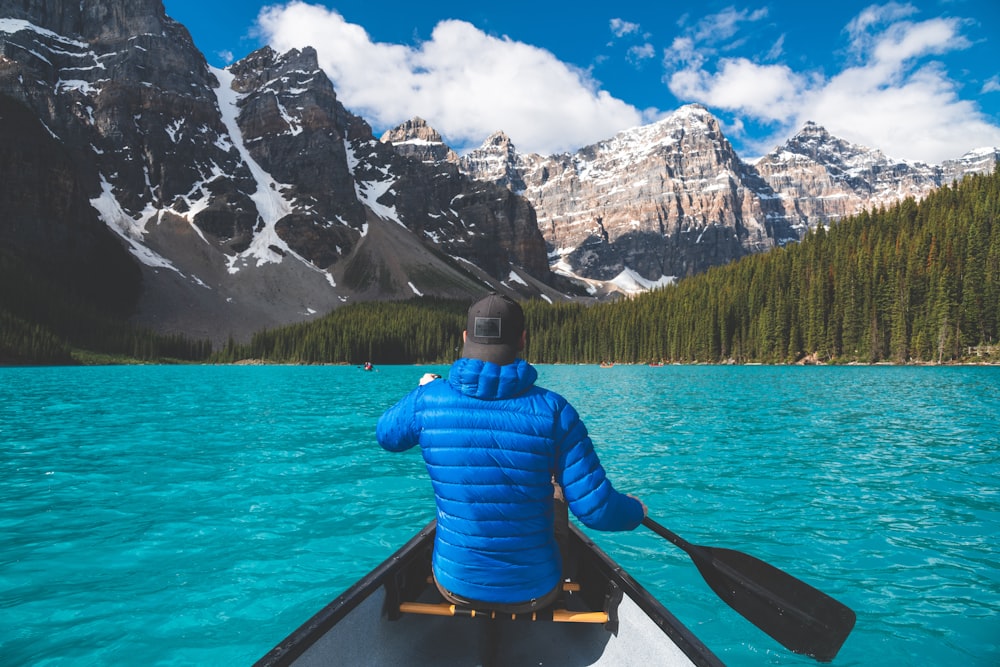 a man in a blue jacket paddling a canoe on a lake