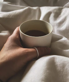 A cozy scene showing a hand wearing layered Korean bracelets next to a cup of tea and a small plant.