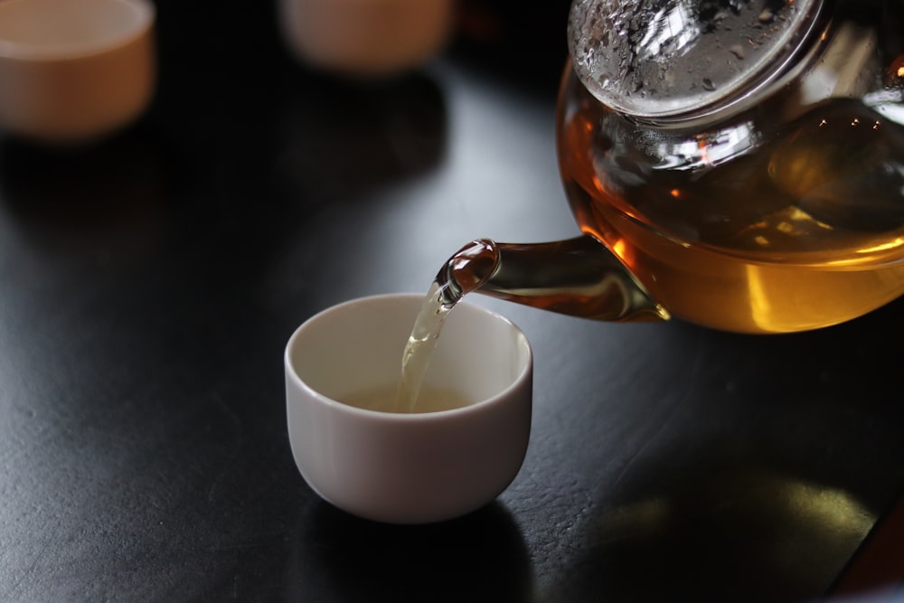 a cup of tea being poured into a teapot