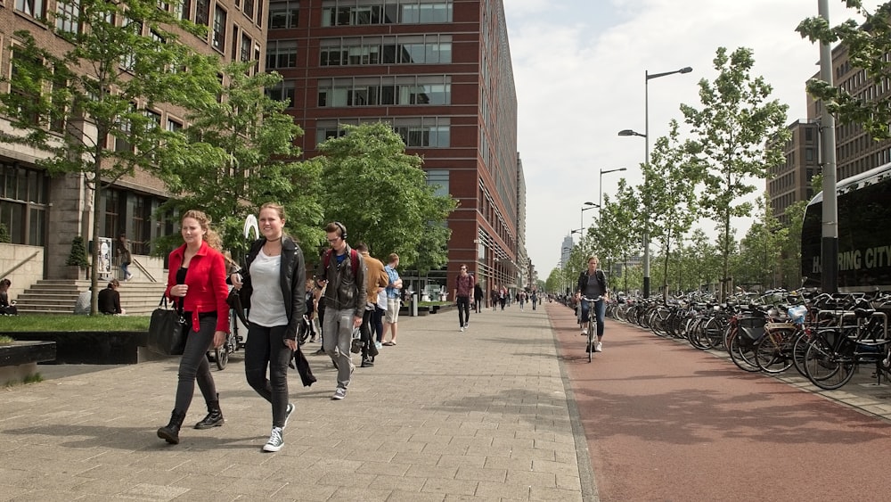 a group of people walking down a sidewalk next to tall buildings