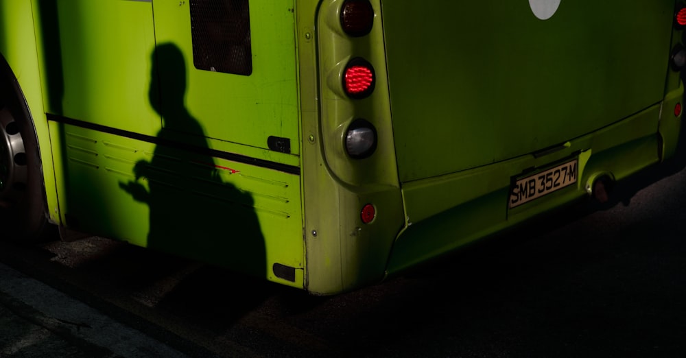 a shadow of a person standing next to a green bus