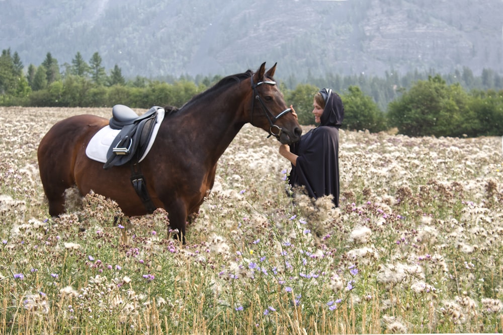 a woman standing next to a brown horse in a field