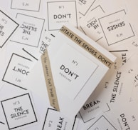 Various perfume labels randomly scattered with prominent texts including 'N°1 DON'T Perfume', 'The Silence Perfume', and 'Break The Silence'. The labels are primarily white with black text, and there is an additional brown wrapper around one of the labels that reads 'AGITATE THE SENSES. DON'T'.