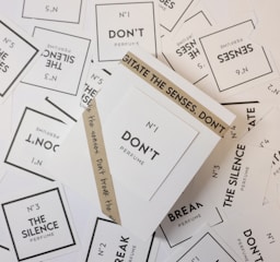 Various perfume labels randomly scattered with prominent texts including 'N°1 DON'T Perfume', 'The Silence Perfume', and 'Break The Silence'. The labels are primarily white with black text, and there is an additional brown wrapper around one of the labels that reads 'AGITATE THE SENSES. DON'T'.