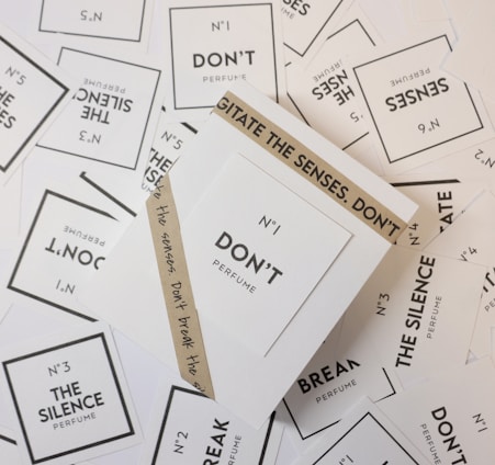 Various perfume labels randomly scattered with prominent texts including 'N°1 DON'T Perfume', 'The Silence Perfume', and 'Break The Silence'. The labels are primarily white with black text, and there is an additional brown wrapper around one of the labels that reads 'AGITATE THE SENSES. DON'T'.