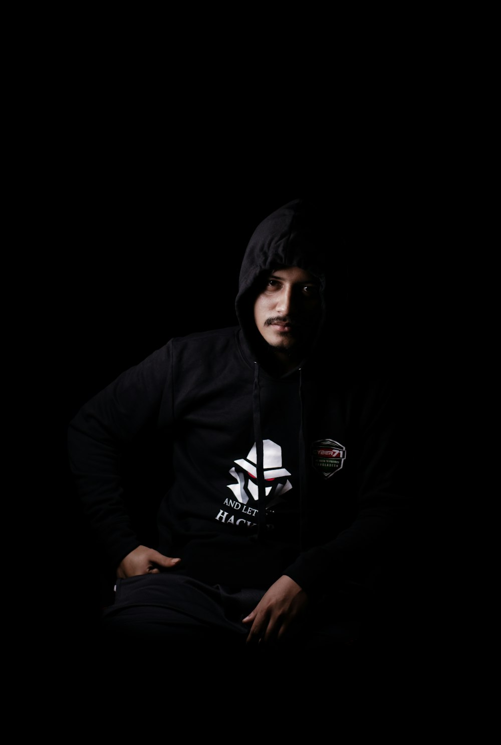 a man sitting in the dark wearing a hoodie