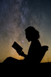 a silhouette of a person reading a book