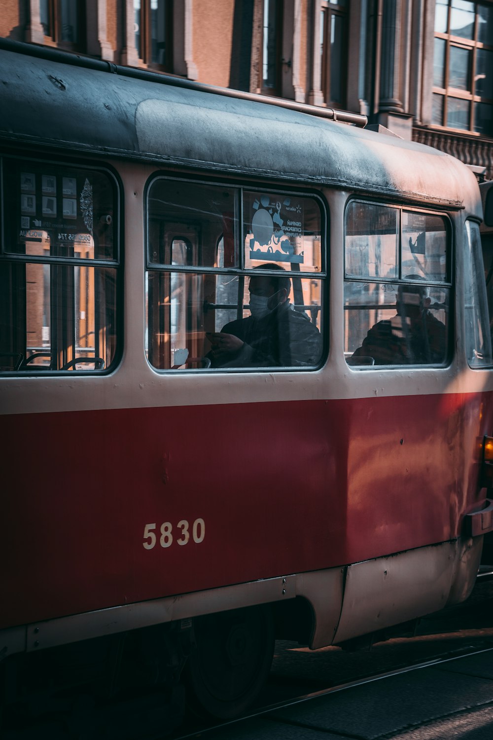 a red and white bus driving down a street next to a tall building