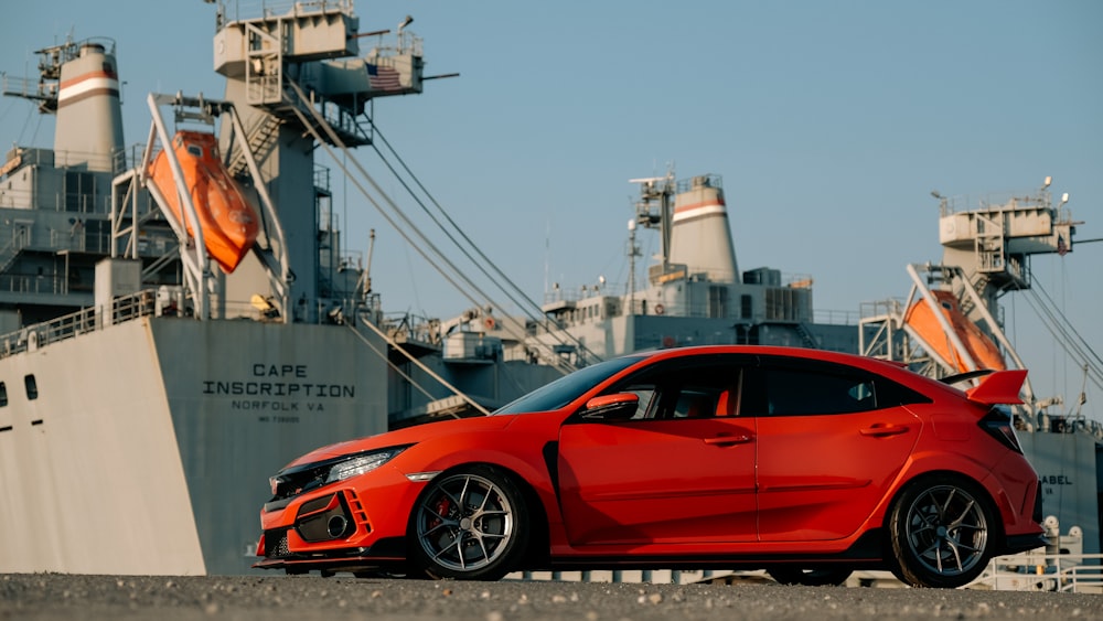 a red car parked in front of a large ship