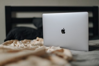 an apple laptop sitting on top of a bed