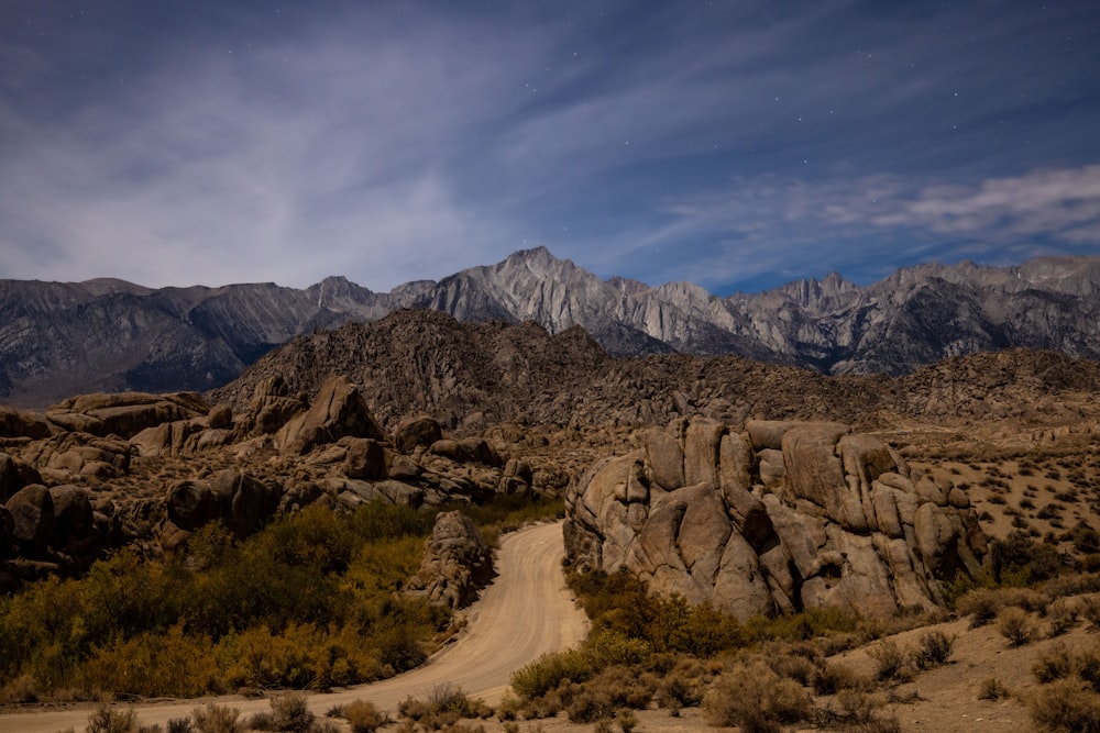 a dirt road surrounded by mountains under a cloudy sky