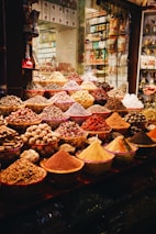 A vibrant display of various spices and herbs in a market setting, featuring bowls and piles overflowing with colorful powders and whole spices. The array is both rich and diverse, capturing the essence of a bustling spice market.