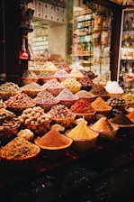 A vibrant display of various spices and herbs in a market setting, featuring bowls and piles overflowing with colorful powders and whole spices. The array is both rich and diverse, capturing the essence of a bustling spice market.