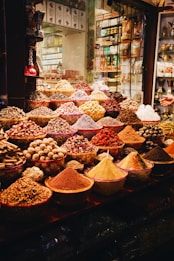 A vibrant display of various spices and herbs in a market setting, featuring bowls and piles overflowing with colorful powders and whole spices. The array is both rich and diverse, capturing the essence of a bustling spice market.