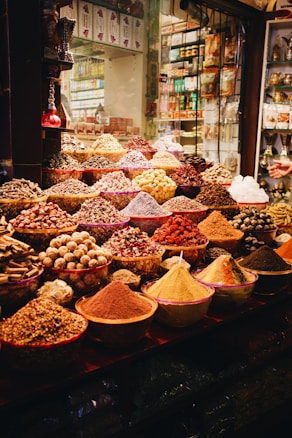 A vibrant display of various spices and herbs in a market setting, featuring bowls and piles overflowing with colorful powders and whole spices. The array is both rich and diverse, capturing the essence of a bustling spice market.