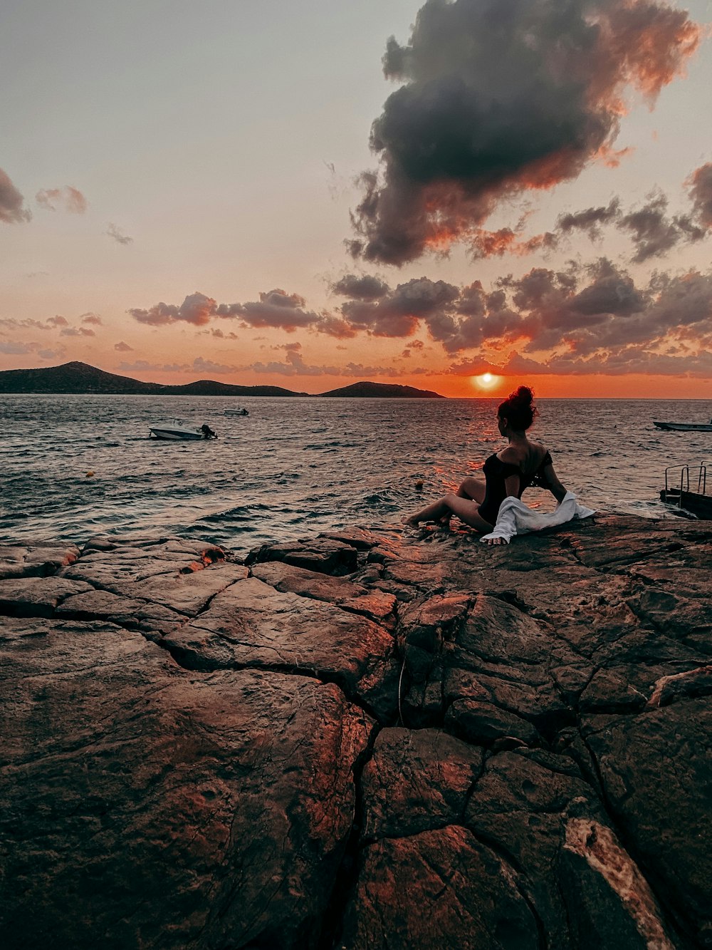 a woman sitting on a rock looking out at the ocean