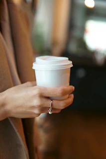 Hand holding a filled coffee cup against the backdrop of the coffee shop interior