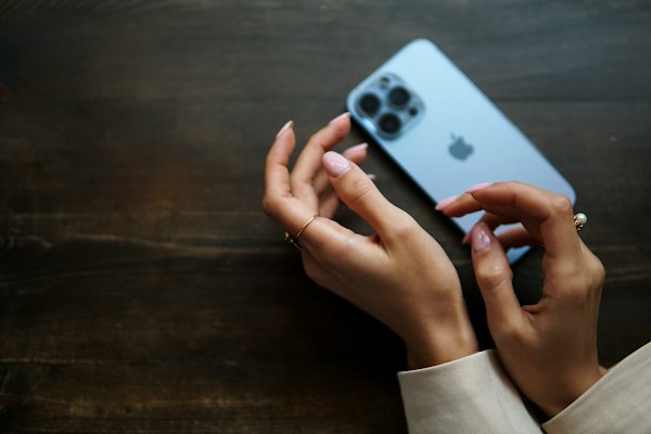 A woman's hands holding a smartphone on a wooden table, deciding what to share in a dating app message