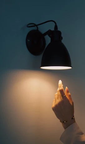 Close-up of a hand adjusting a stylish lamp with UV detail accents on a dark background.