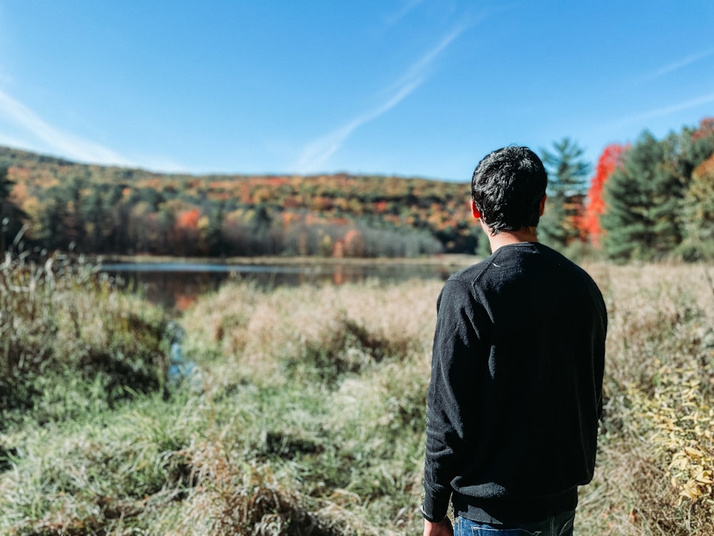 a man standing in a field looking at a lake