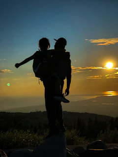 A serene outdoor scene with a mother and child silhouette against a sunset sky.