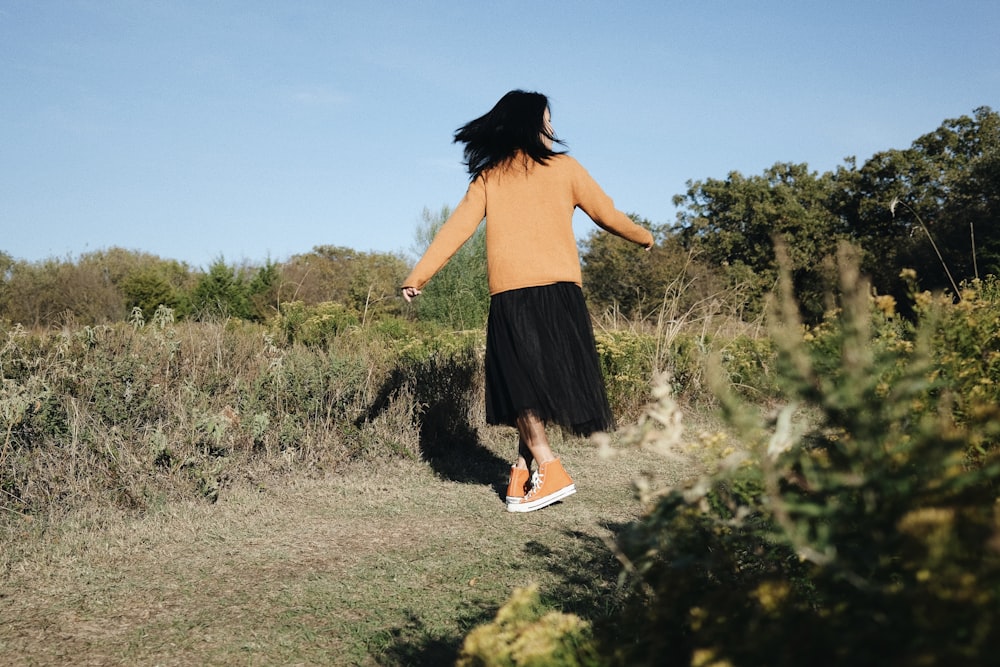 a woman walking down a dirt road in a field