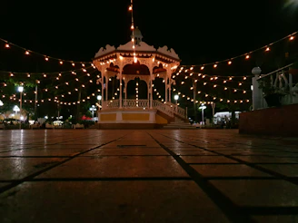 A lively garden party under a hardtop gazebo surrounded by lush greenery and string lights in the evening.