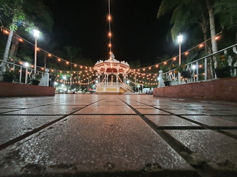 Wide shot of a wooden garden gazebo decorated with fairy lights in the evening.