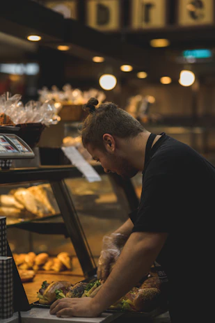 A chef preparing a quick gourmet sandwich behind the counter at γευστική πνοή.