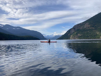 a person in a canoe on a lake with mountains in the background