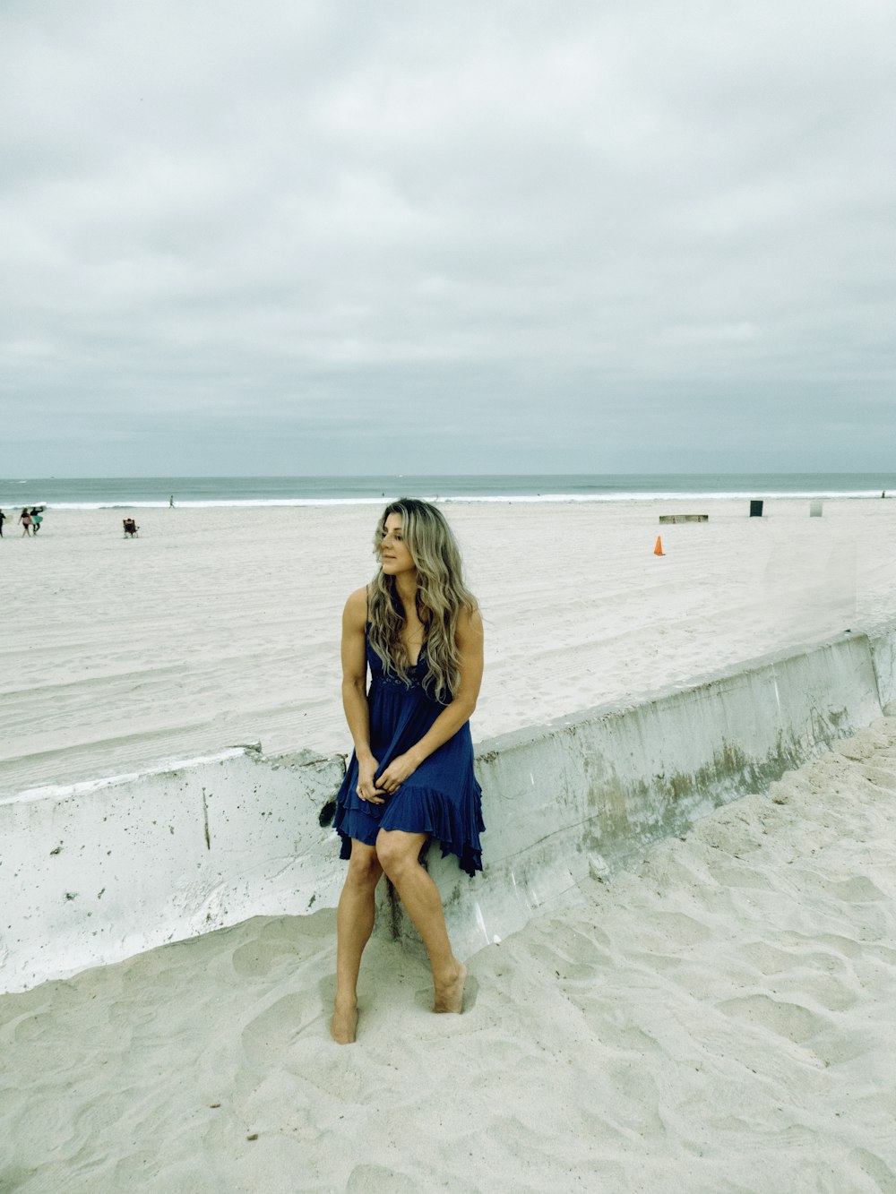 a woman in a blue dress sitting on a wall at the beach
