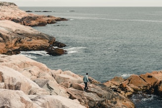 a man standing on top of a rocky cliff next to the ocean