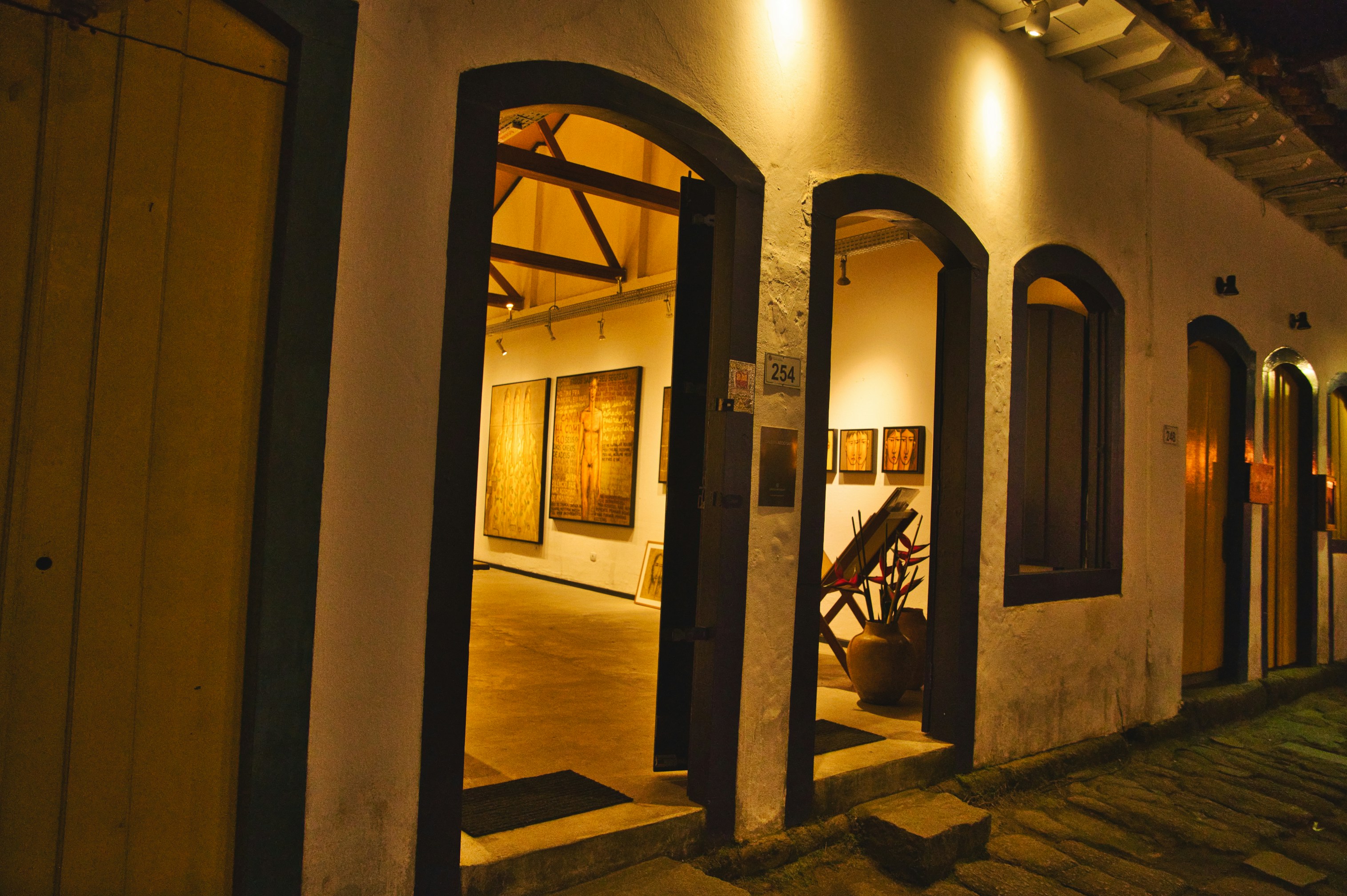 Evening gallery opening with visitors viewing large-scale nature-inspired artworks under warm lighting