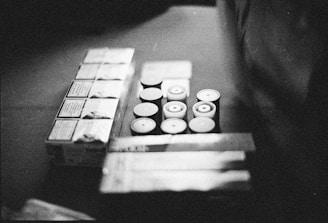 Several rolls of film and boxes are arranged on a surface in a monochrome setting. The image appears grainy, adding a vintage or retro feel.