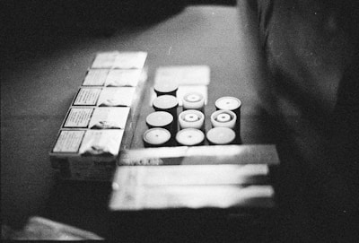 Several rolls of film and boxes are arranged on a surface in a monochrome setting. The image appears grainy, adding a vintage or retro feel.