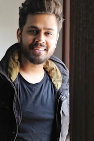 A smiling man gently massaging beard oil into his beard in front of a mirror, sunlight highlighting the natural shine.