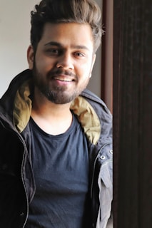 A smiling man gently massaging beard oil into his beard in front of a mirror, sunlight highlighting the natural shine.