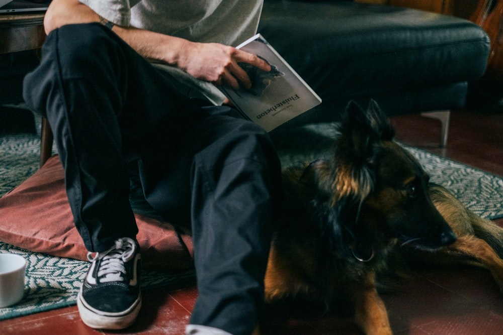 a man sitting on the floor reading a book with his dog
