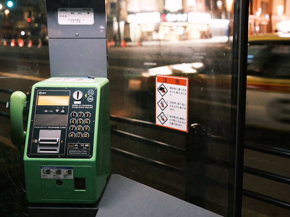 a green pay phone sitting next to a parking meter