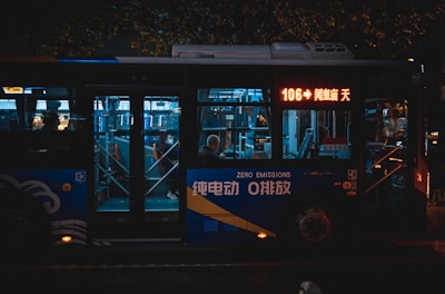 A city bus at night with illuminated signage and interiors. It is marked as a zero emissions vehicle. Passengers inside are visible through the windows, and the bus displays the route number 106 on a digital screen.