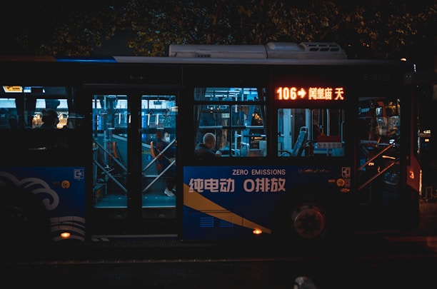 A city bus at night with illuminated signage and interiors. It is marked as a zero emissions vehicle. Passengers inside are visible through the windows, and the bus displays the route number 106 on a digital screen.