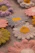 Close-up photo of a soft pastel-hued crocheted flower resting gently on a lavender cloth.