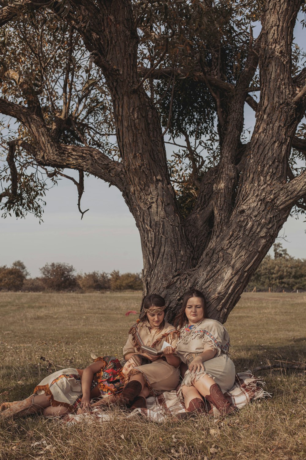 two women sitting under a tree in a field